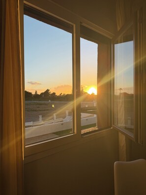 Ein Zimmer mit großem Fenster, das auf einen Parkplatz und einen Sonnenuntergang blickt.