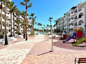 A resort with a pool, palm trees, and a playground. - Casa de Momentos - Pool, Sun & Golf - Los Alcázares (Los Alcázares)
