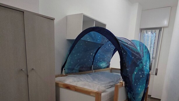 Une chambre avec un lit superposé, une armoire et un petit espace nuit fermé, surmonté d’un ciel de lit en tissu orné de motifs étoilés.