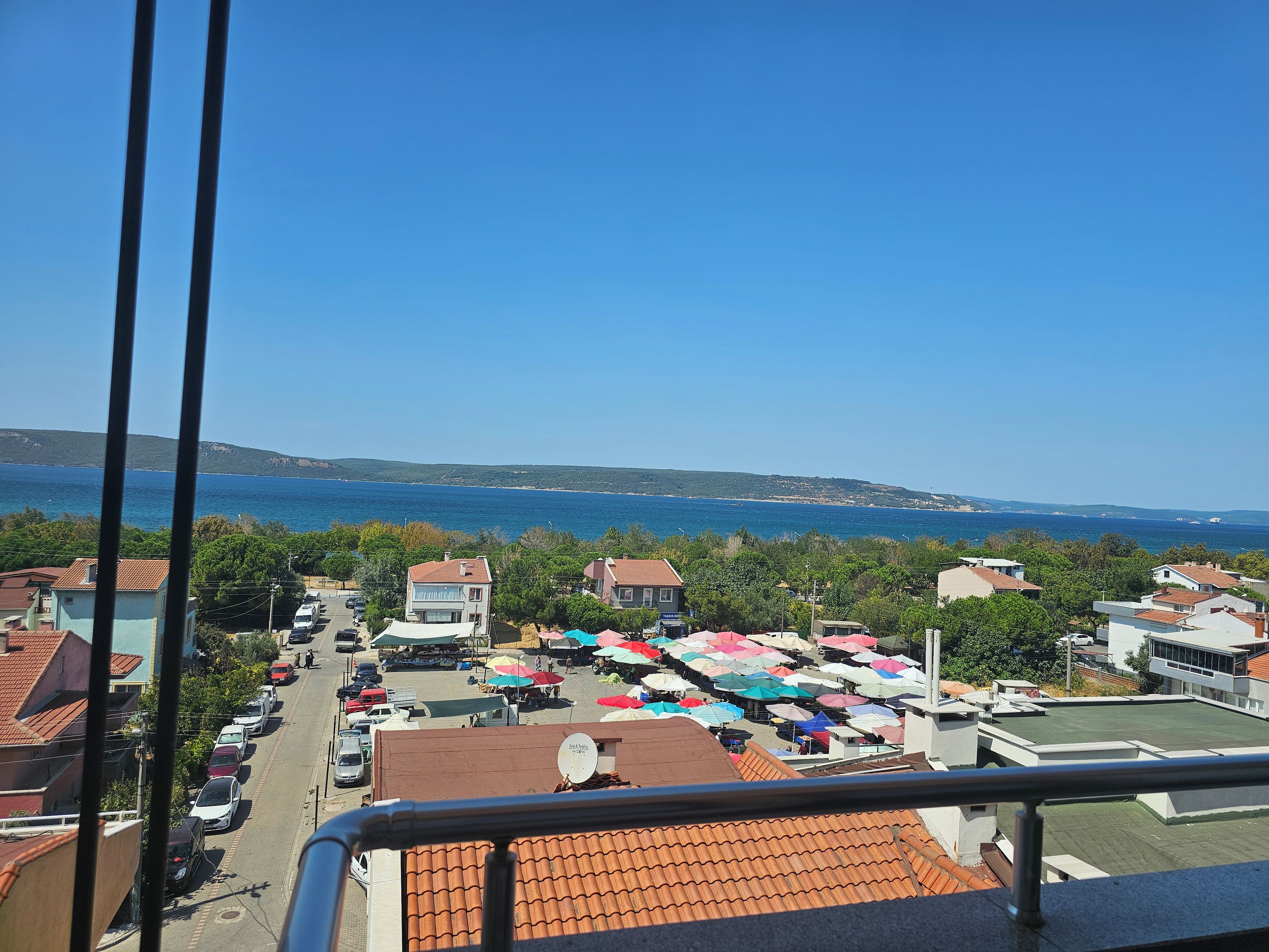 A coastal town with a view of the sea, parked cars, and a market area with colorful umbrellas.