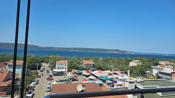 Un pueblo costero con vista al mar, autos estacionados y una zona de mercado con sombrillas de colores.