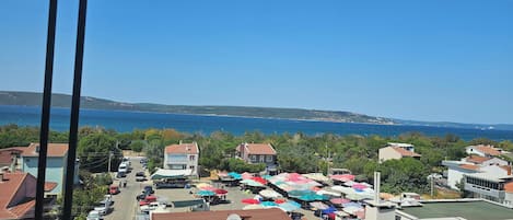 A coastal town with a view of the sea, parked cars, and a market area with colorful umbrellas.