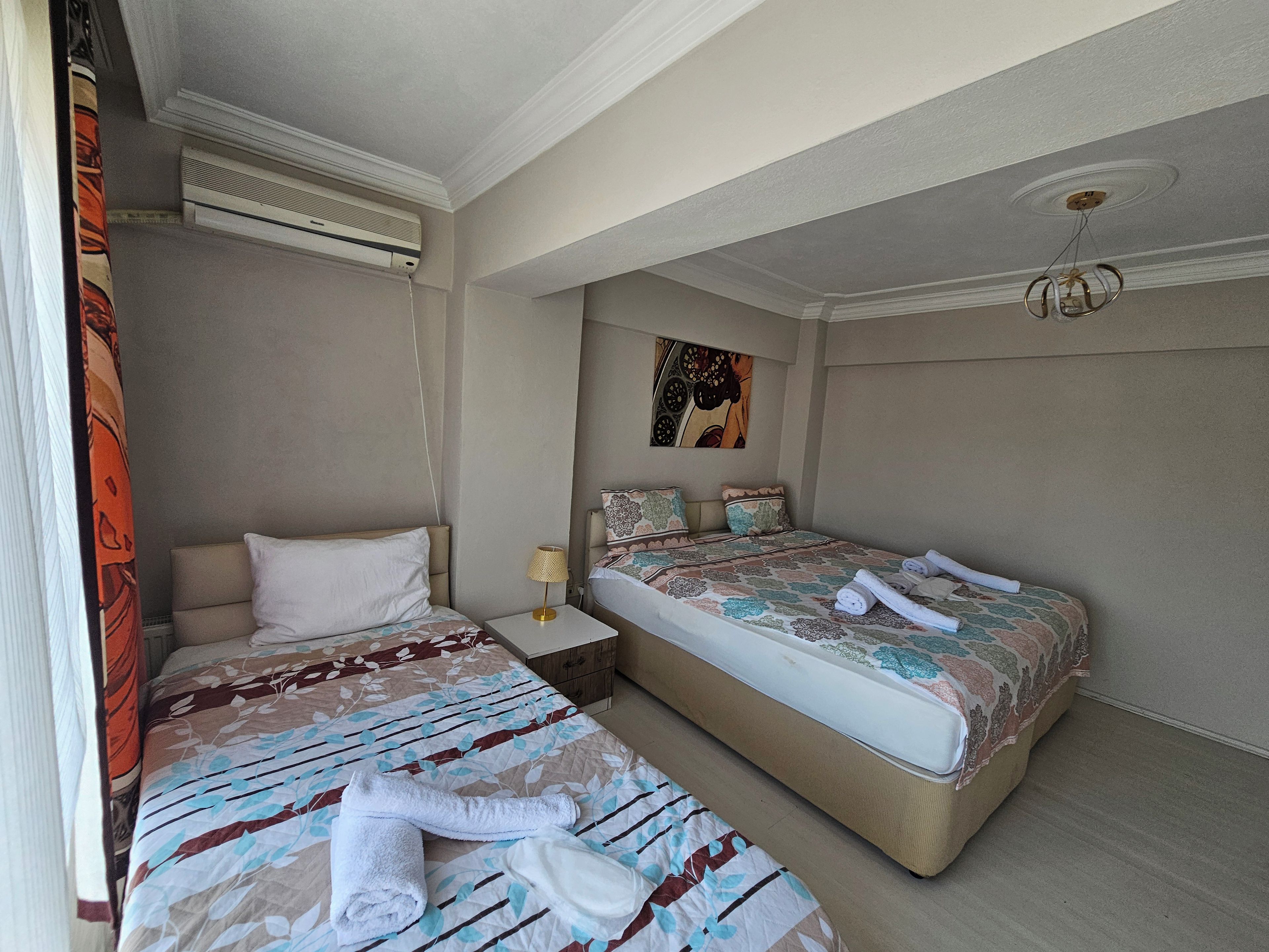Una habitación de hotel con dos camas, un ventilador de techo, un equipo de aire acondicionado y un cuadro en la pared.