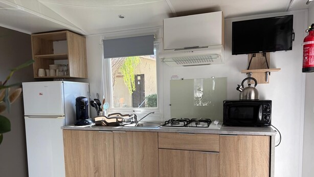 Uma cozinha compacta com geladeira, fogão, micro-ondas e TV fixada na parede.