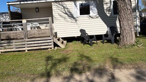 Uma casa móvel térrea com quintal cercado, uma árvore e área de estar externa.