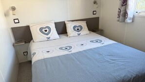 Cama bem arrumada com almofadas estampadas em formato de coração e um edredom com padrão azul e branco.