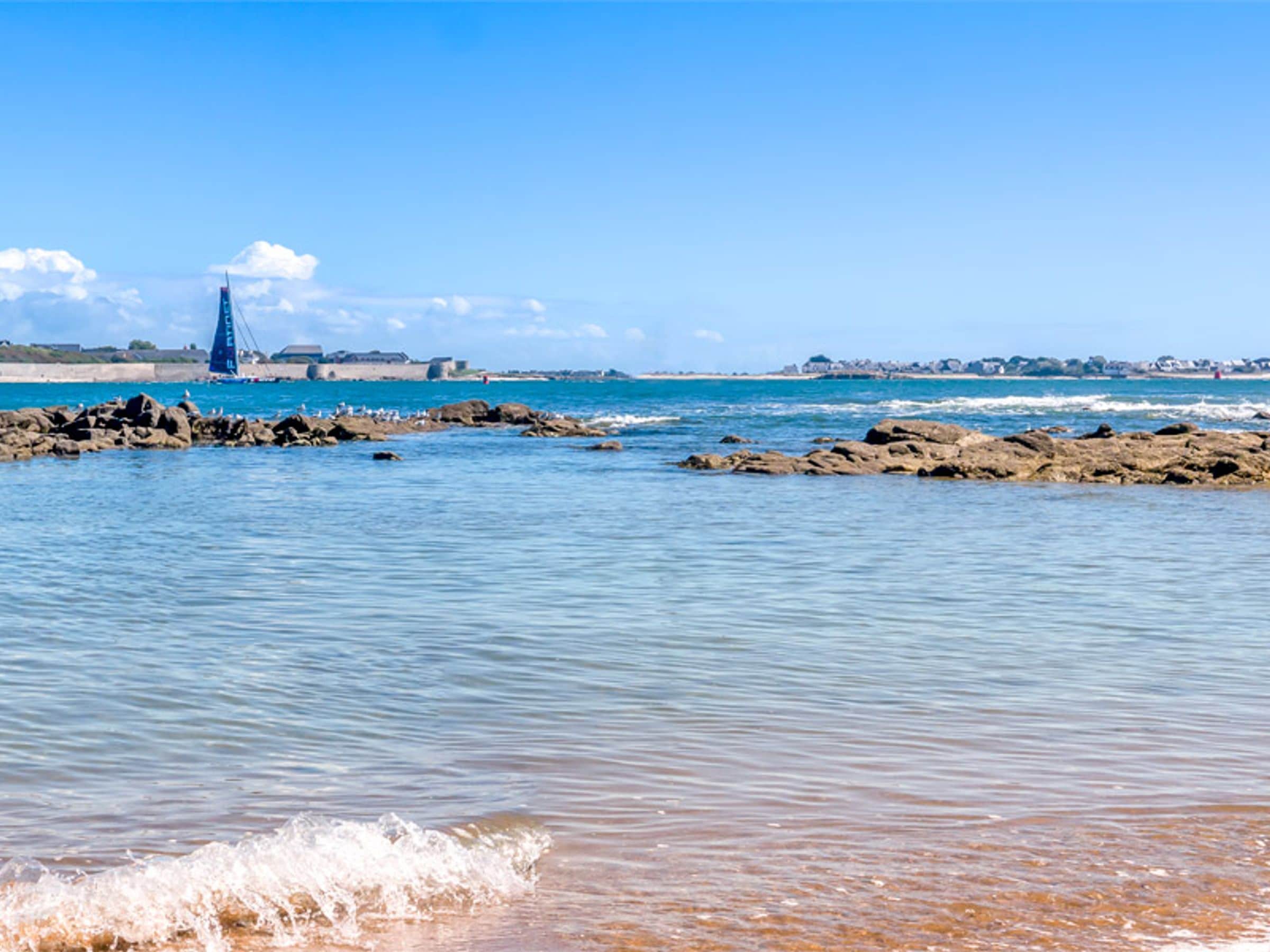 Paesaggio costiero con scogliere rocciose, acque calme e una barca a vela.