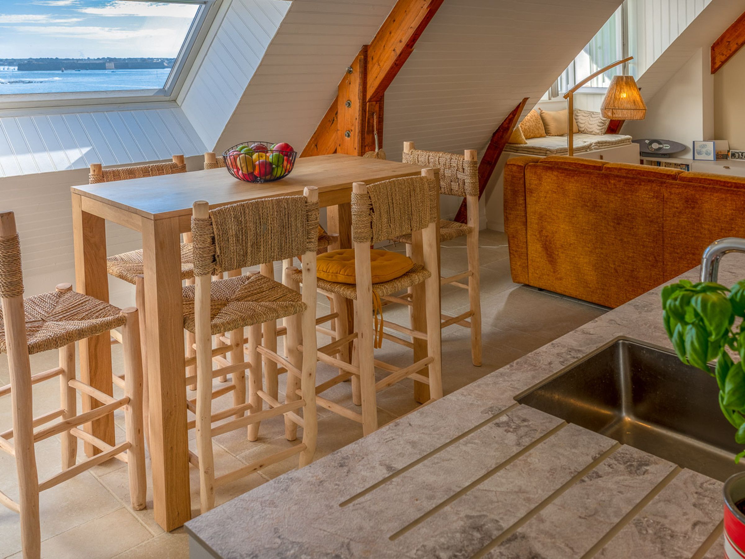 A modern kitchen with a wooden table and chairs, a kitchen island, and a view of the sea through a skylight.