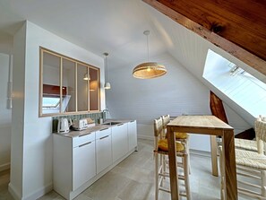 Een moderne keuken met witte kasten, een grote spiegel en een eethoek met een houten tafel en stoelen.