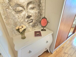 Eine weiße Kommode mit Spiegel und Buch, ein Blumenstrauß und ein großes abstraktes Gemälde an der Wand.