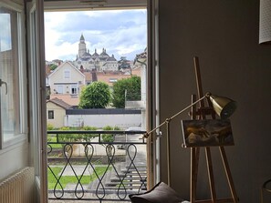 Una habitación con vista a un edificio histórico, un balcón con barandilla de metal y un caballete con una pintura.