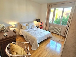 Ein Schlafzimmer mit einem Bett, Nachttischlampen, einem Sessel und einem Fenster mit Vorhängen.
