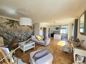 A spacious living area with a large sofa, a coffee table, and a decorative lamp. There is a kitchen in the background with modern appliances and a dining area. - Modern apartment cathedral view - 4 guests (Périgueux)