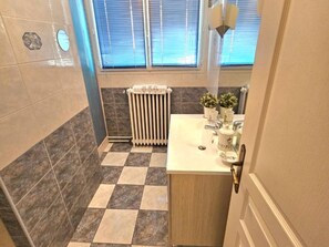 Ein Badezimmer mit Schachbrettboden, einem Heizkörper, einem Waschbecken mit Dekoration und einem Fenster mit Jalousien.