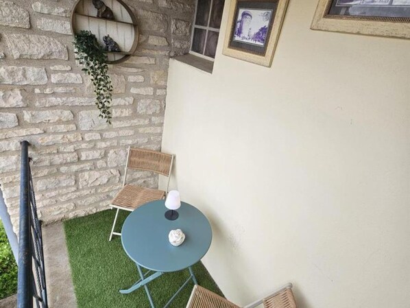 Een stenen muur, een ronde tafel met twee stoelen, en een lijst met een afbeelding aan de muur.