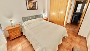 A bedroom with a bed, a nightstand, a lamp, a wardrobe, and a bathroom visible through an open door. - 2-bedroom apartment with parking, pool, and close to the beach in Roses (Roses)