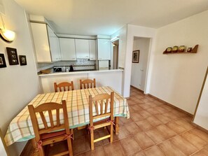 A dining area with a table and chairs, a kitchen in the background, and a hallway leading to another room. - 2-bedroom apartment with parking, pool, and close to the beach in Roses (Roses)