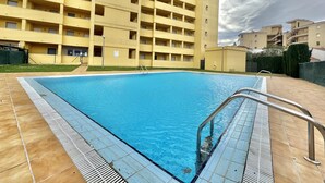A swimming pool with a tiled deck, surrounded by a multi-story yellow building with balconies. - 2-bedroom apartment with parking, pool, and close to the beach in Roses (Roses)