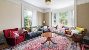 A spacious living room with a large window, a red armchair, a sofa set, and a round coffee table.