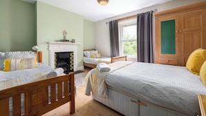 A bedroom with two beds, a fireplace, a window with curtains, and a wooden wardrobe. - Large 9-Bed Wicklow Retreat • Sleeps 18+ • Valley Views • Sauna • Parking (Rathdrum)