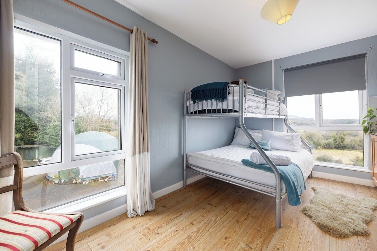 Une chambre avec un lit superposé, de grandes fenêtres, une chaise et un tapis.