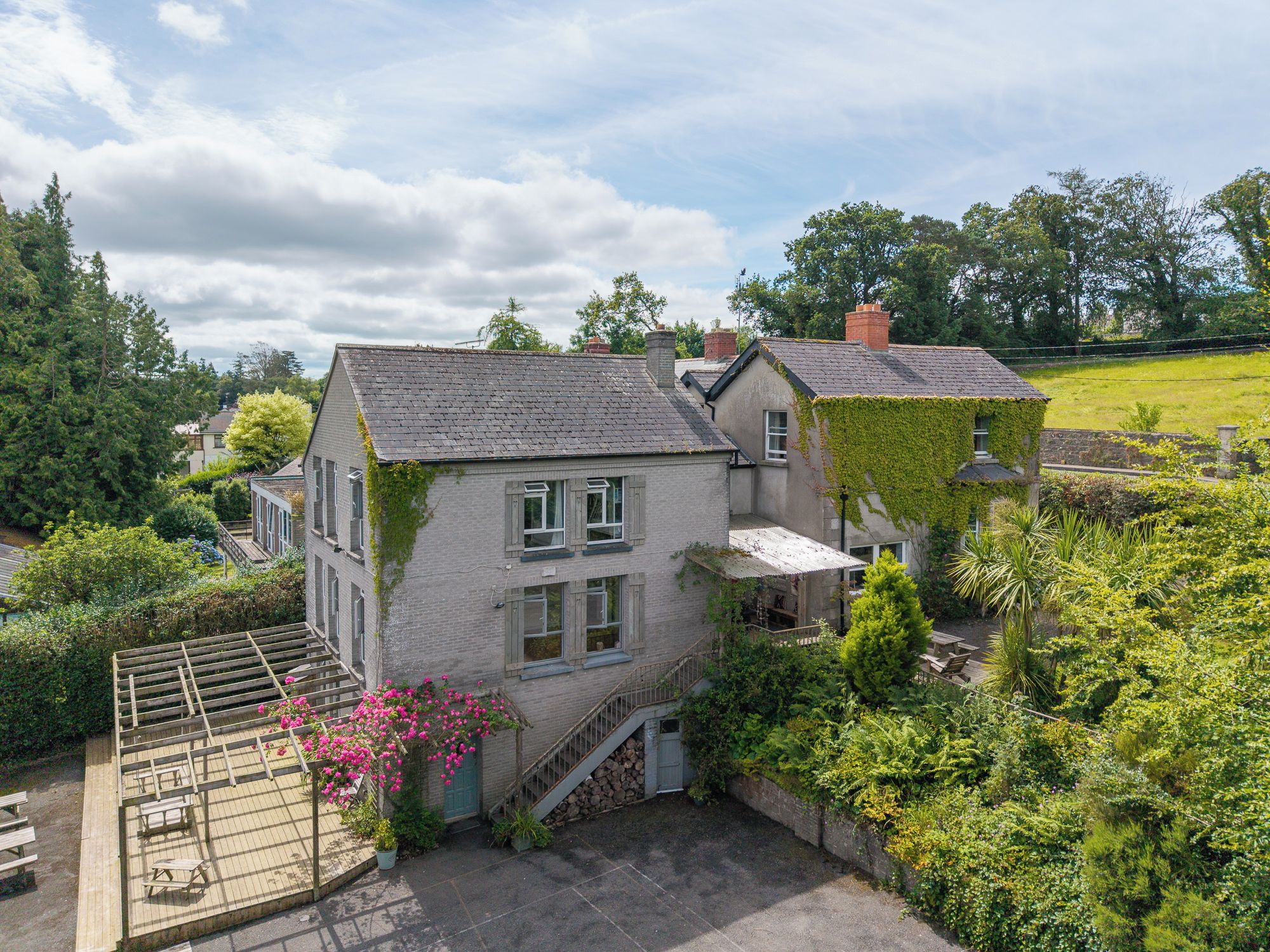 A two-story house with a garden, a staircase, and a patio with outdoor furniture.