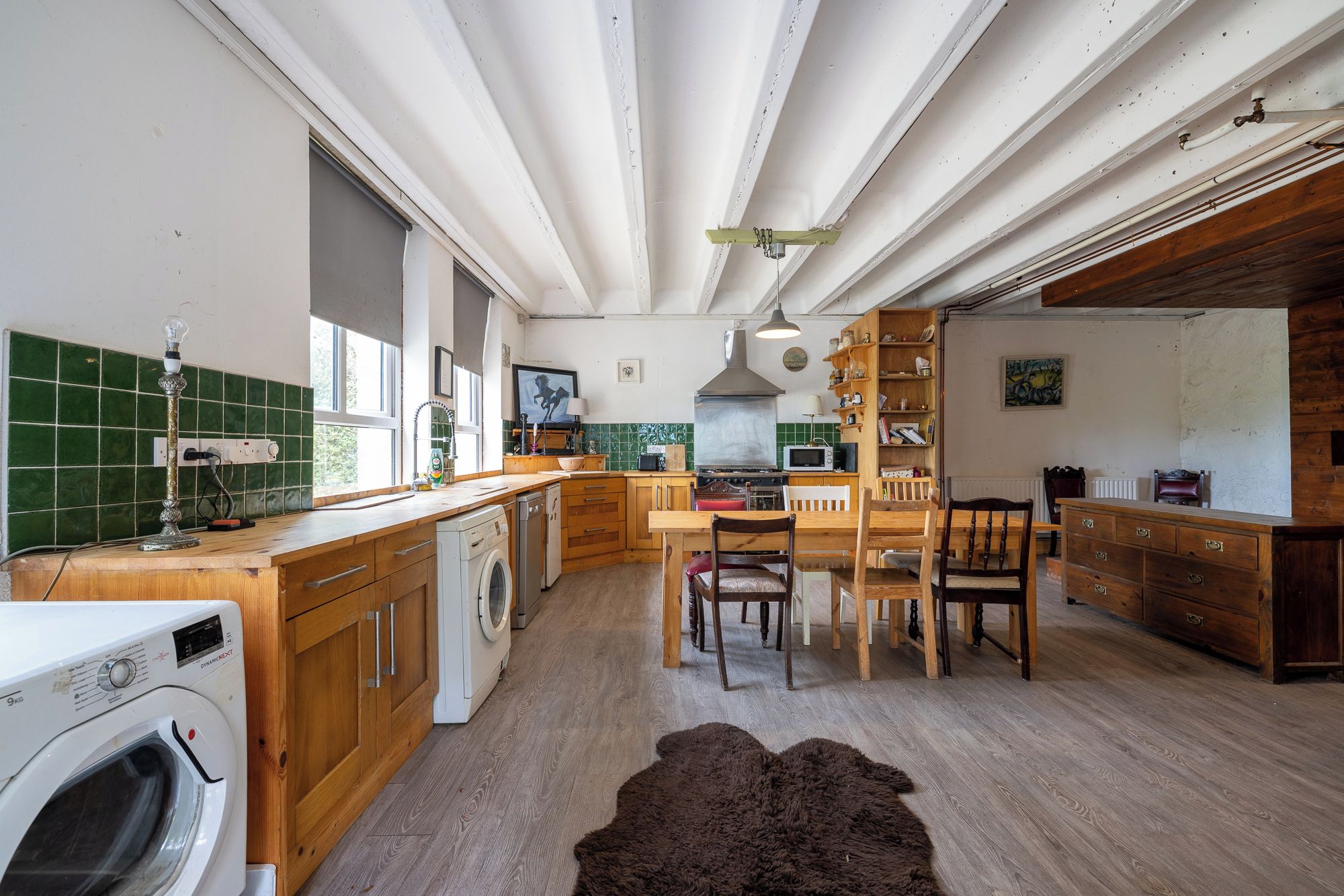 Una cocina con armarios de madera, horno empotrado, microondas y comedor con mesa y sillas.