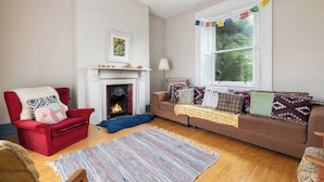 A living room with a fireplace, a red armchair, a brown sofa, and a large window with a view of greenery. - Large 9-Bed Wicklow Retreat • Sleeps 18+ • Valley Views • Sauna • Parking (Rathdrum)
