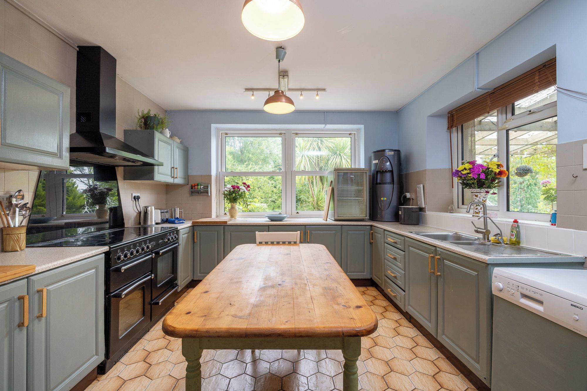 Een keuken met een houten tafel, een fornuis, een koelkast en een raam met uitzicht op groen.