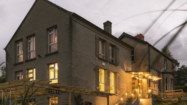 A two-story building with a balcony, a staircase, and a small garden area. - Large 9-Bed Wicklow Retreat • Sleeps 18+ • Valley Views • Sauna • Parking (Rathdrum)