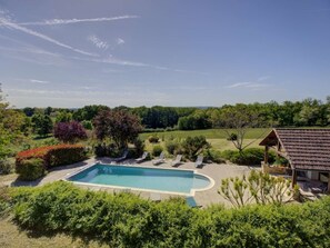 A swimming pool with lounge chairs, surrounded by greenery and a view of the countryside.