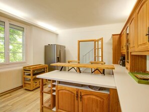 A kitchen with wooden cabinets, a white countertop, a refrigerator, and a window with blinds.