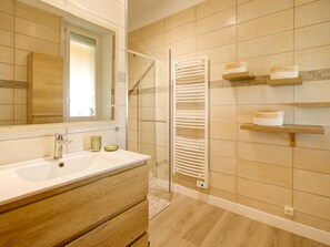 A bathroom with a white sink, wooden vanity, a glass shower enclosure, and a towel rack.