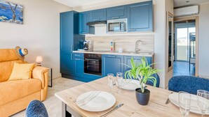 A modern kitchen with blue cabinets, a microwave, and an oven. There's a dining table set with plates, cutlery, and glasses. - Apartment with AC, sea view - 4 guests (Le Lavandou)