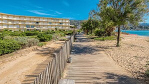 A coastal hotel with a wooden boardwalk leading to the beach, surrounded by greenery and a clear blue sky. - Apartment with AC, sea view - 4 guests (Le Lavandou)