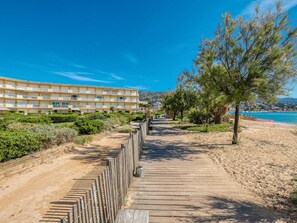 A coastal hotel with a wooden boardwalk leading to the beach, surrounded by greenery and a clear blue sky. - Apartment with AC, sea view - 4 guests (Le Lavandou)