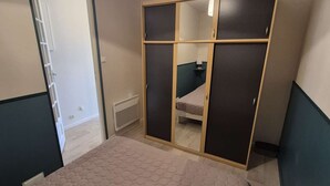 Ein Schlafzimmer mit einem Bett, einem Schrank mit Spiegelüren, einem Heizkörper und einer Tür zu einem anderen Raum.