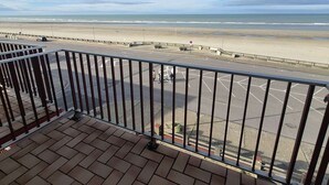 Blick von einem Balkon auf einen Strand mit einer Straße und Parkplatz.
