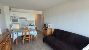 Ein kompakter Wohnbereich mit Küchenzeile, Essbereich und einem dunkelgrauen Sofa.
