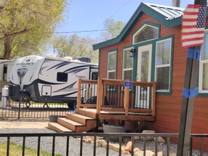A small cabin with a porch, a sign indicating 'Deluxe Cabin 2,' and an RV parked nearby.