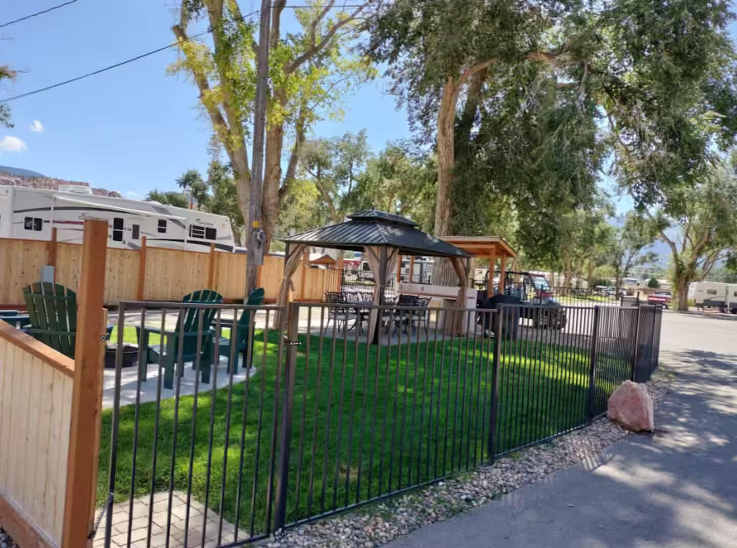 A fenced outdoor area with a gazebo, picnic tables, and green chairs.