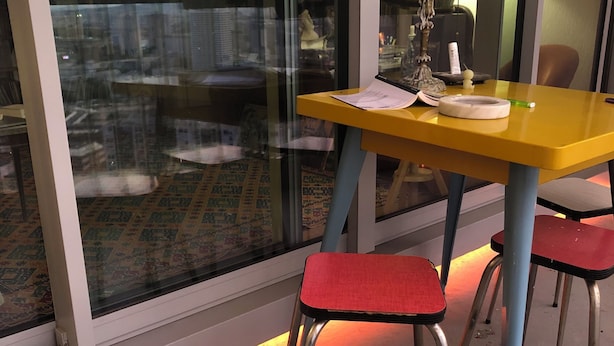 Ett rum med ett gult bord, två röda stolar, en lampa och en utsikt genom ett stort fönster.