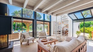 Ein modernes Interieur mit Holzbalkendecke, großen Fenstern, einem Pool und Sitzgelegenheiten im Freien.