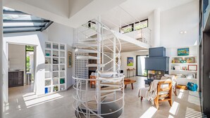 Ein großzügiger Wohnbereich mit einer zentralen Wendeltreppe, einem Kamin und einem großen Fenster für natürliches Licht.