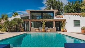 Ein modernes Haus mit Swimmingpool, großen Fenstern und Sitzgelegenheit im Freien.