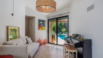 Una sala de estar moderna con un sofá, un piano, una mesa roja y un gran ventanal con vistas a una piscina.