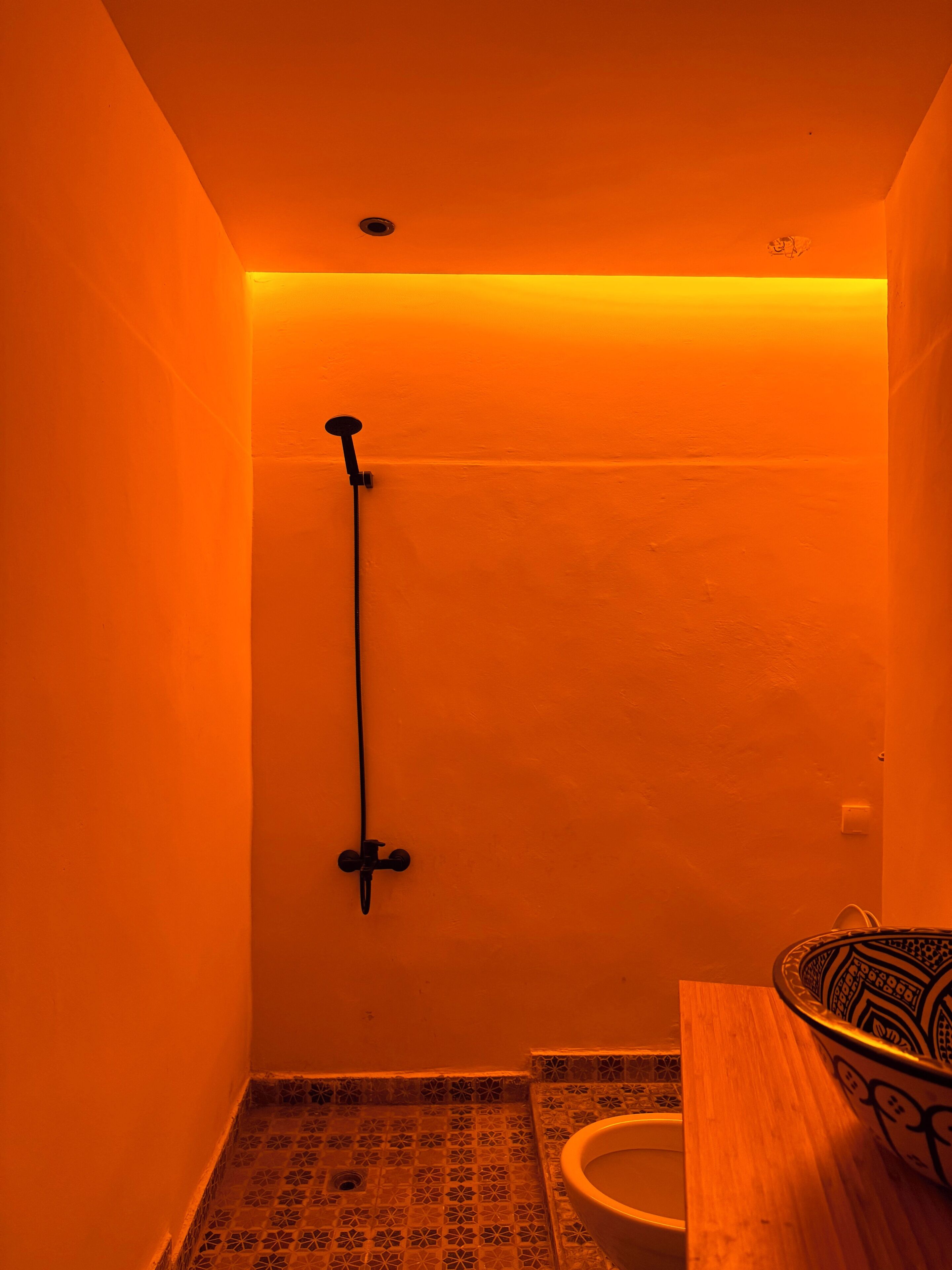 A small, orange-lit bathroom with a shower, a toilet, and a decorative bowl on the counter.