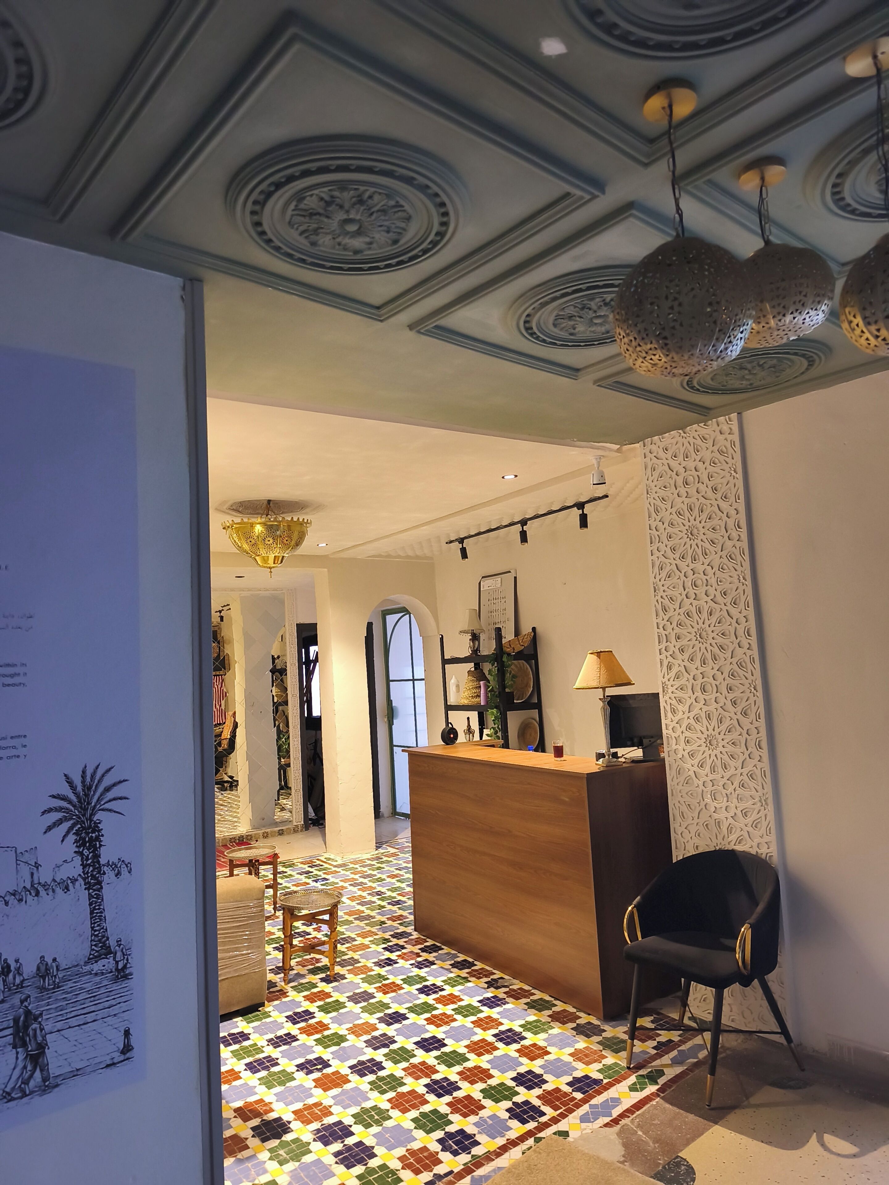 Un vestíbulo de hotel con una recepción, una silla negra, un suelo estampado y un techo decorativo.