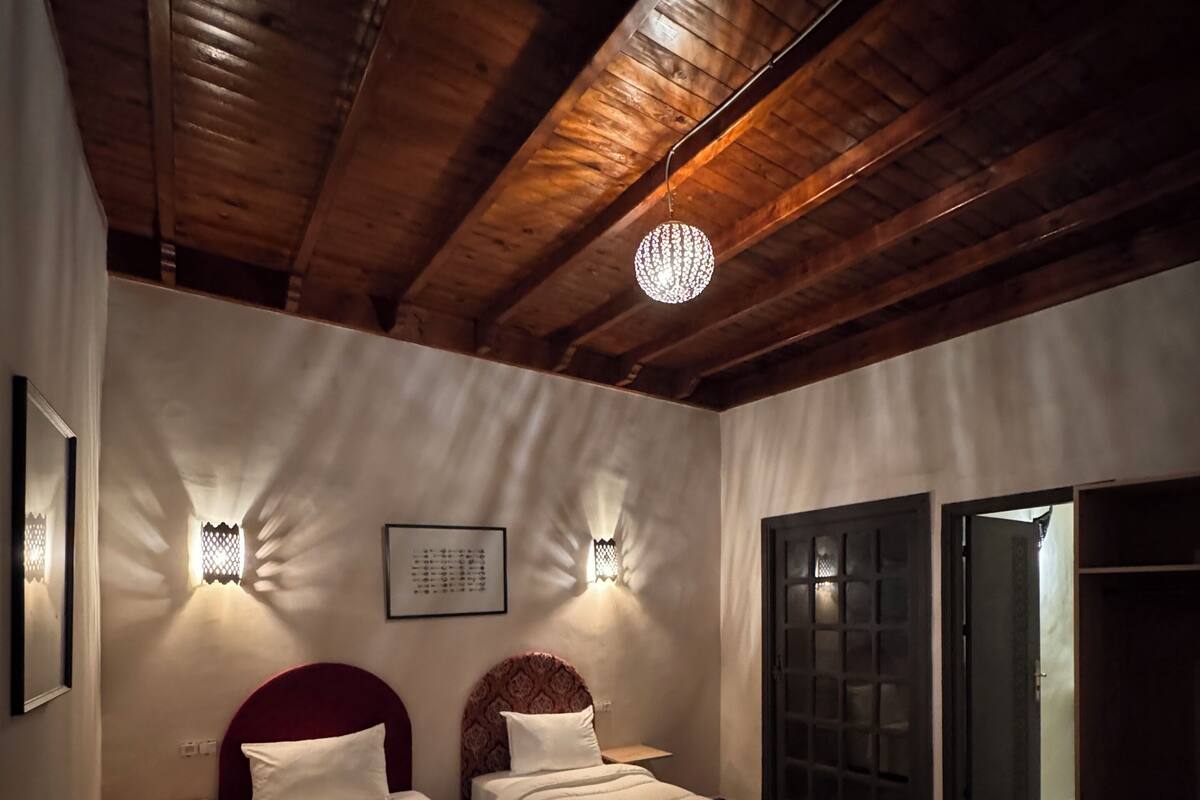 Una habitación con dos camas, techo de madera y un candelabro.