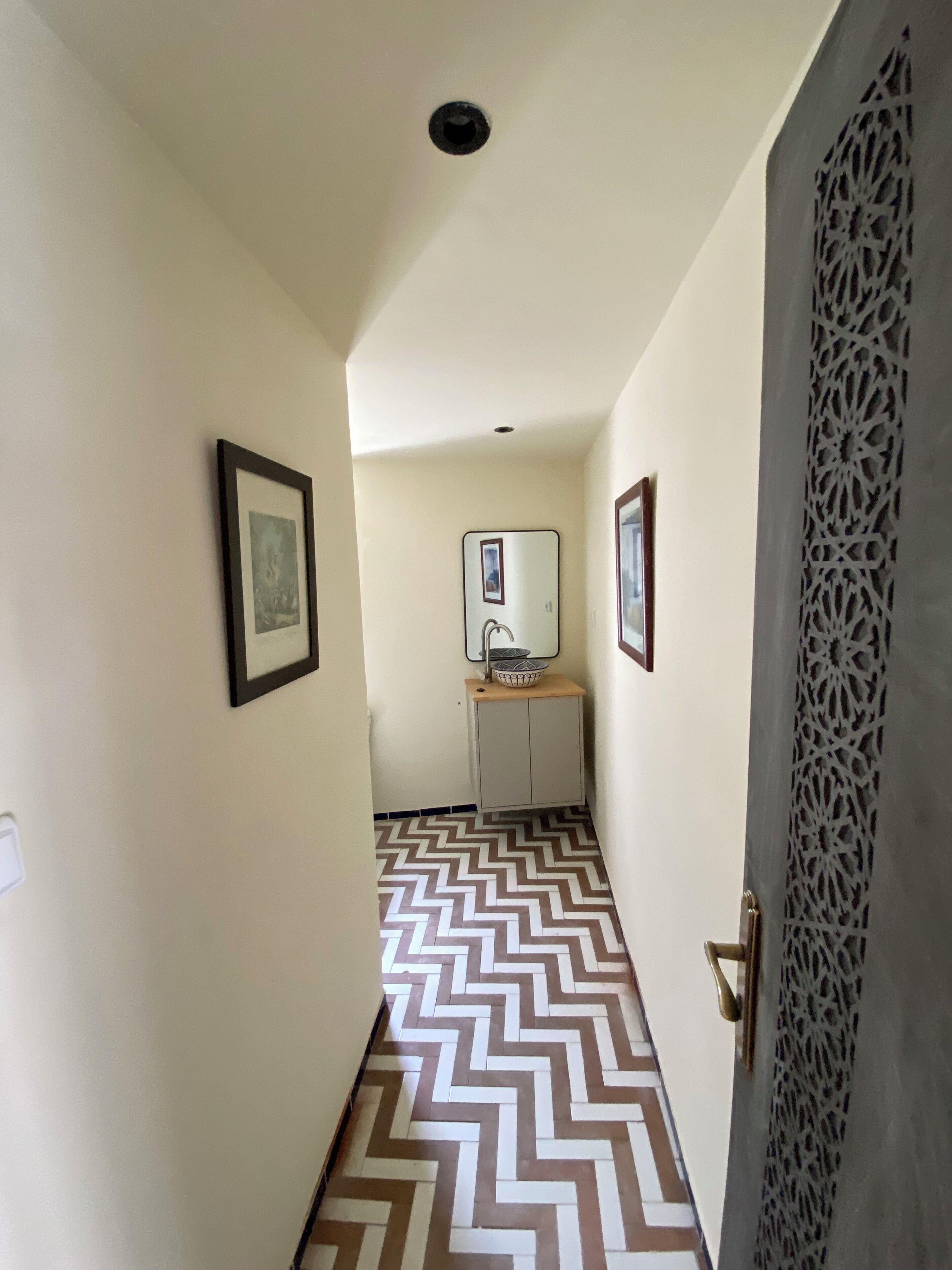 Un couloir doté d’un revêtement de sol à motifs, une porte au décor travaillé et un petit meuble agrémenté d’un miroir.